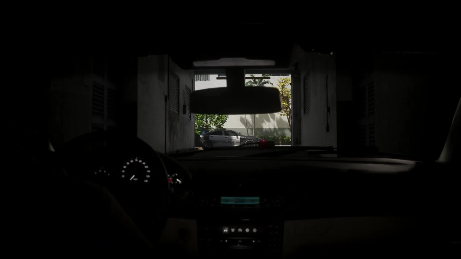 Viewed from a car waiting in a dim garage, a police sedan sits on the sunny street just past the exit.