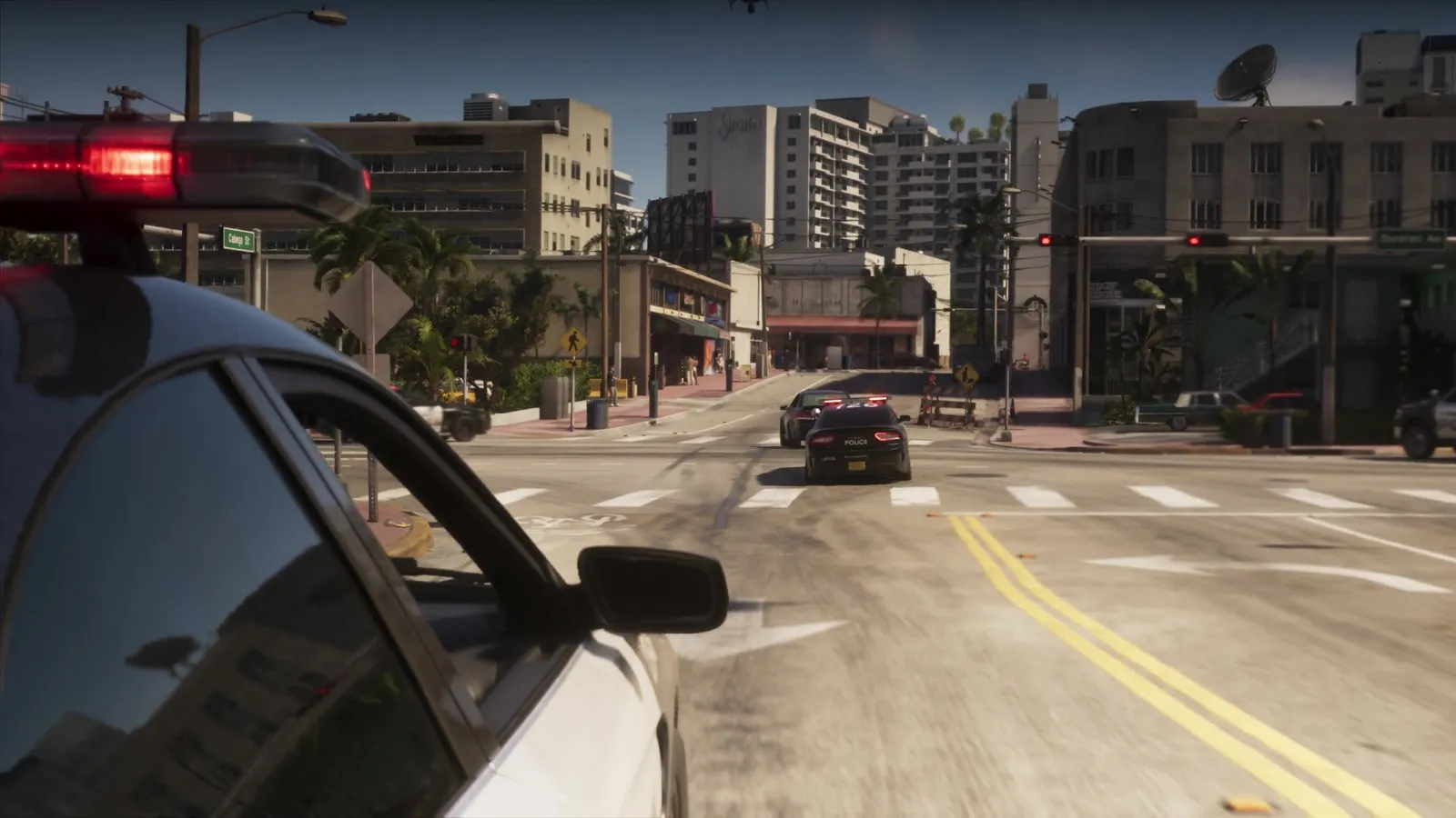 A black police car follows a dark sedan across a downtown intersection as other police cars move in.