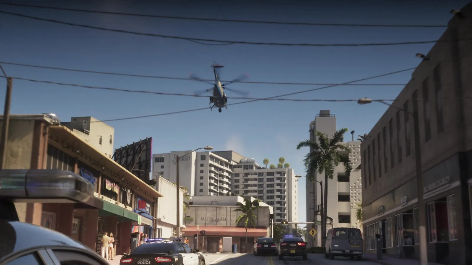 A helicopter flies low over police cars with lights on driving down a city street.
