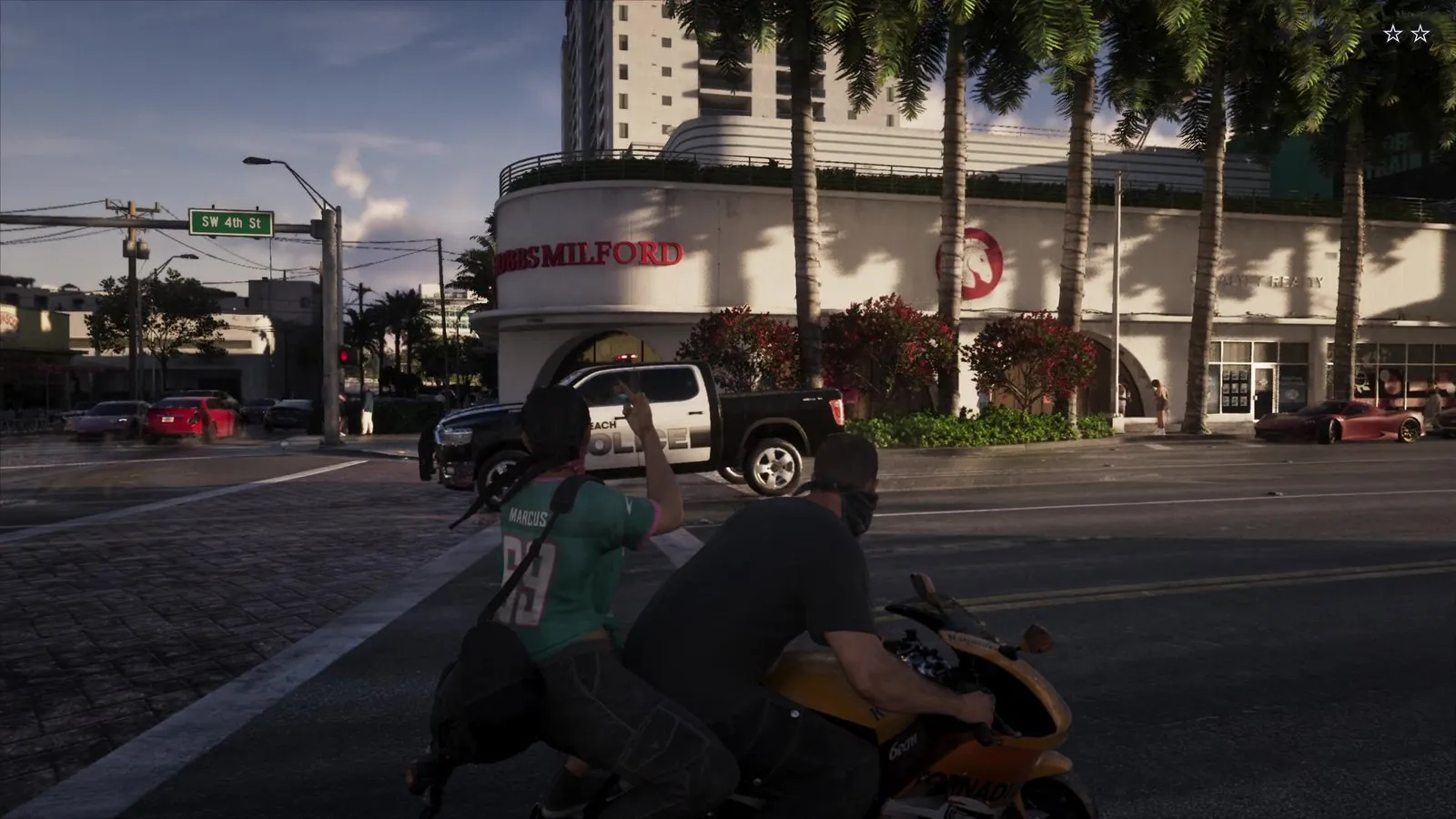 A masked passenger on a motorcycle gestures at a black and white police pickup crossing the intersection in front of them.