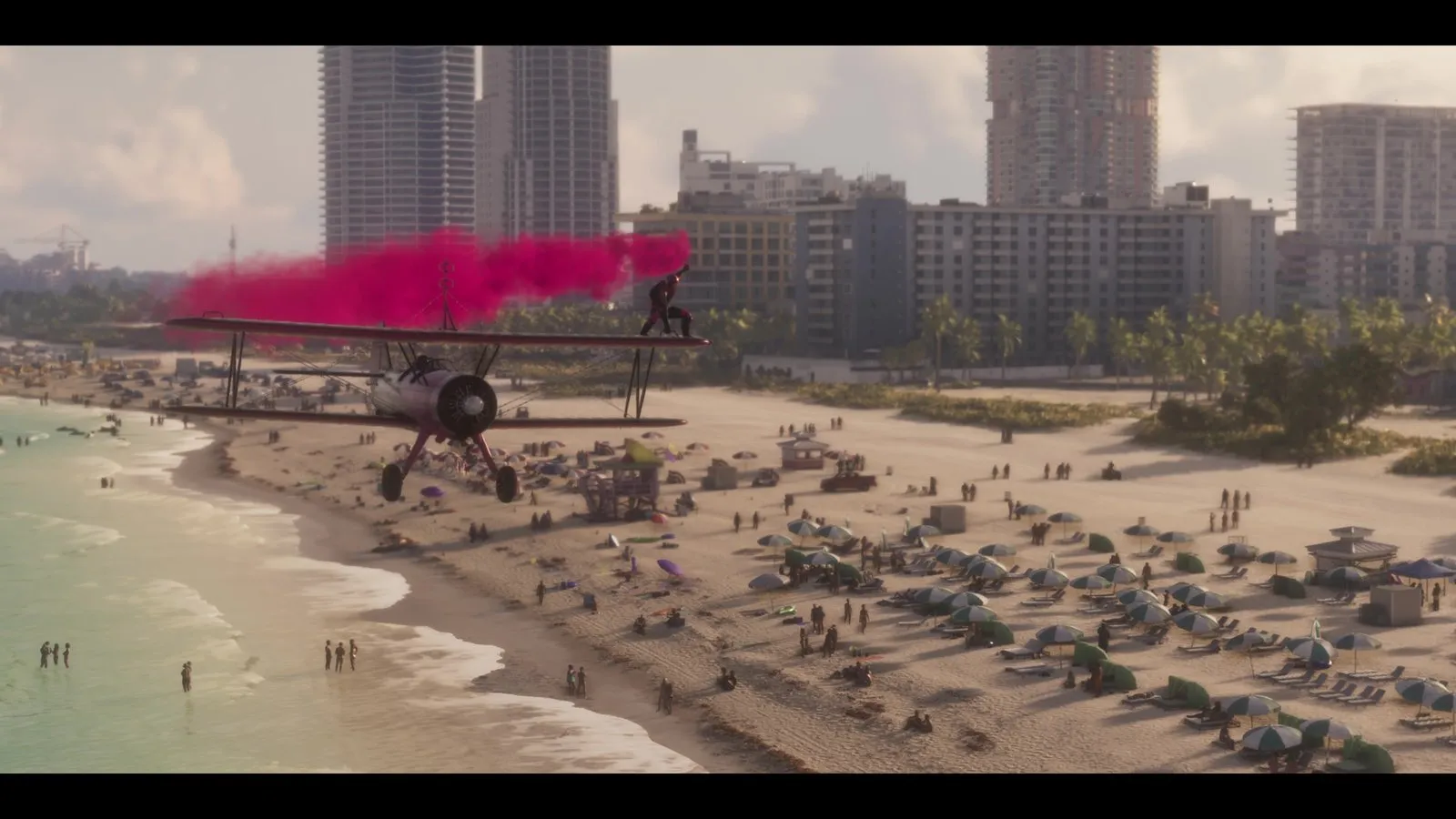 A red pickup sits on the sand near a lifeguard tower as a biplane with a wing walker trails pink smoke above the beach.