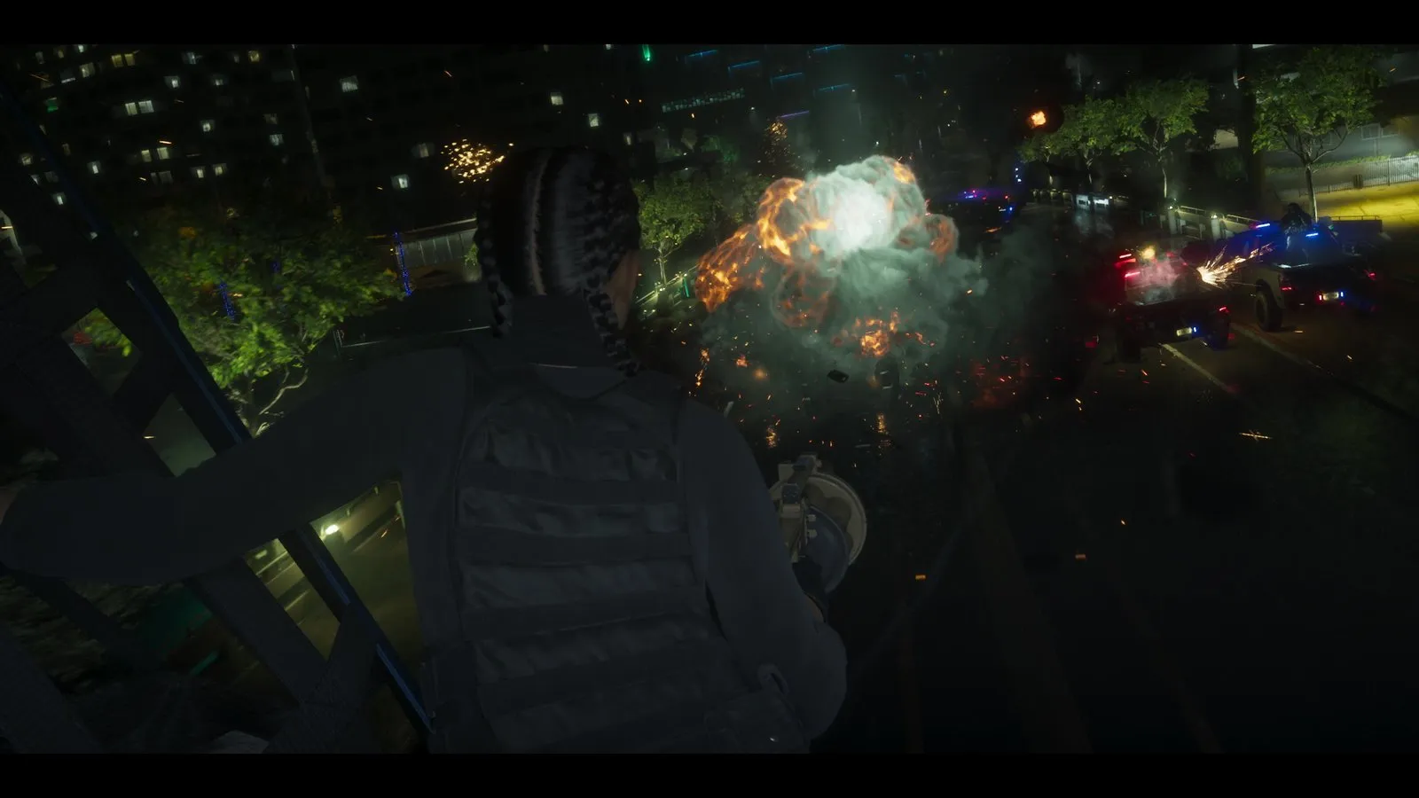 A shooter in a tactical vest fires from a balcony as an explosion erupts among police vehicles on the street below.