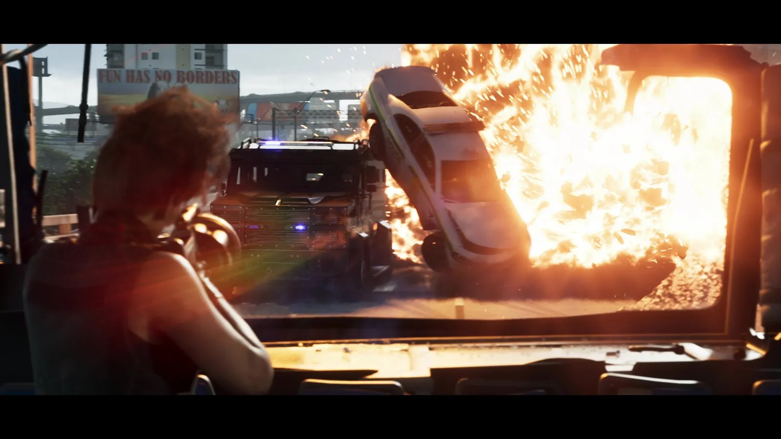A police sedan is thrown into the air by a fireball beside an armored truck during a highway chase.